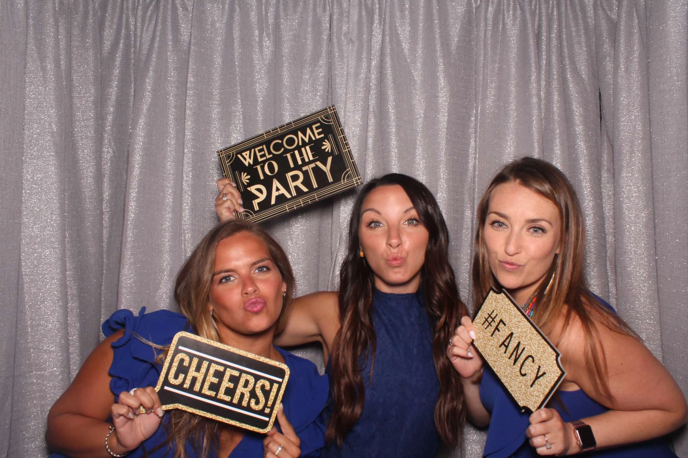 three girls pose with photo booth props against silver backdrop